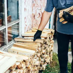 Mężczyzna w rękawiczkach układa drewno. Chcesz wiedzieć, jak obliczyć m3 drewna? Oto stosy gotowe do pomiaru.