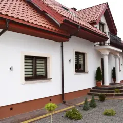 Biały dom z brązowym dachem i cokołem. Eleganckie schody prowadzą do wejścia.