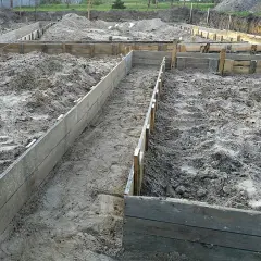 Wykonano wykopy pod fundamenty. Drewniane szalunki wyznaczają kształt przyszłego budynku na piaszczystym terenie budowy.