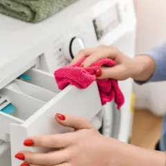 Kobieta czyści szufladę pralki, która zaczęła wydzielać zapach jak szambo.