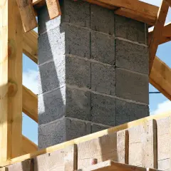 Solidny fundament pod komin systemowy, wznoszony z bloczków betonowych, otoczony drewnianą konstrukcją dachu.