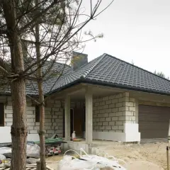 Budowa domu w toku. Widać białe płyty styroduru przy ścianach, które będą izolacją. Obok stoi przyczepa kempingowa.
