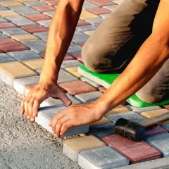 Ręce układają kolorową kostkę brukową, tworząc wzór. Praca wymaga precyzji i cierpliwości.