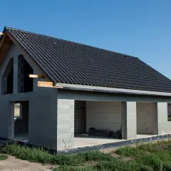 Dom w stanie surowym otwartym, z dachem pokrytym czarną dachówką, gotowy na dalsze prace budowlane.