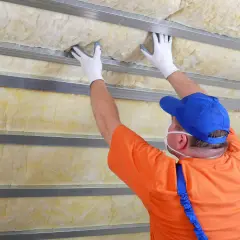 Pracownik montuje wełnę mineralną, wykonując ocieplenie garażu blaszanego.