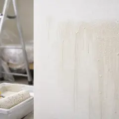 Ślady po malowaniu pod światło, widoczne na chropowatej ścianie. Obok wałek w kuwecie i drabina.