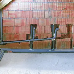 Instalacja hydrauliczna z rurami, zapewniająca minimalny spadek dla rury 160. Ściana z pustaków ceramicznych, podłoga betonowa, widoczne drewniane elementy konstrukcji dachu.
