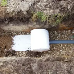 Budowa drenażu: rura drenarska owinięta geowłókniną, otoczona żwirem i ziemią, gotowa do zasypania.