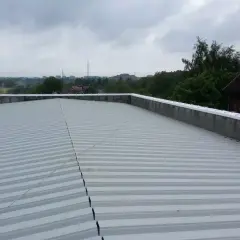 Szary, lekki dach płaski z blachy falistej, z widokiem na miasto w tle.
