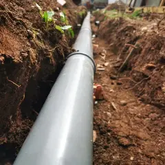 Wykonanie drenażu rozsączającego: szary rów z rurą, przygotowany do odprowadzania wody.