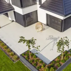 Nowoczesny taras z płyt betonowych, otoczony zielenią i nowoczesną architekturą. Idealne miejsce na relaks.