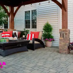 Jak zbudować taras? Wygodny zestaw wypoczynkowy, stolik i piękne kwiaty na wybrukowanym patio.