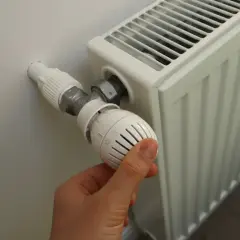 Dłoń reguluje termostat grzejnika. Sezon grzewczy od kiedy do kiedy zależy od pogody i przepisów.