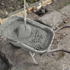 Taczka z betonem i łopatą czeka na wykonanie zbrojenia ławy fundamentowej.
