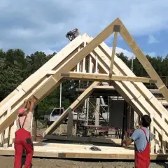 Budowa dachu z drewnianych wiązarów. Pracownicy montują elementy konstrukcji, pokazując różne rodzaje wiązarów dachowych.