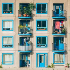 Elegancka loggia i balkon z niebieskimi ramami okiennymi, pełne zieleni i suszącego się prania, tworzą barwny obraz miejskiego życia.