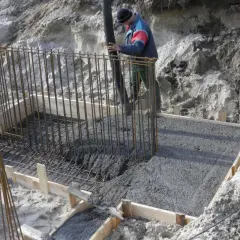 Betonowanie fundamentów. Pracownik wylewa beton do szalunku zbrojonego. Beton można lać do ok. +5°C.