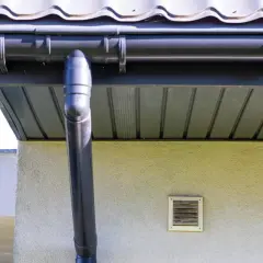Montaż podbitki stelaż pod rynną i pionowym odpływem. Widać fragment dachu, okapu i wentylacji ściennej.