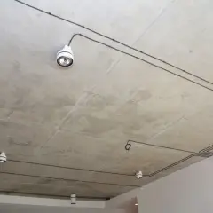 Nowoczesna instalacja elektryczna natynkowa na betonowym suficie z kilkoma białymi oprawami oświetleniowymi.