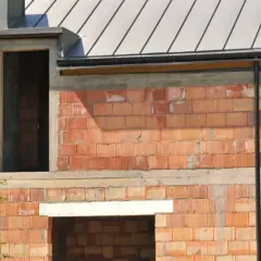 Budowa domu w toku. Widoczne ocieplenie nadproża pod rolety, ściany z pustaków ceramicznych i metalowy dach.