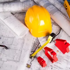 Plany budowlane, żółty kask, miarka i czerwone domki symbolizują projektowanie i minimalną szerokość działki budowlanej.