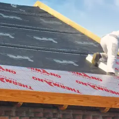 Pracownik montuje materiał izolacyjny na dachu, zapewniając ocieplenie dachu od zewnątrz.