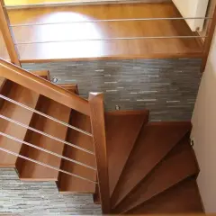 Eleganckie drewniane schody z metalową balustradą, prowadzące do górnego poziomu. Kamienna ściana stanowi stylowe tło, pokazując, jak zakończyć ostatni stopień schodów.