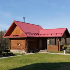 Drewniany domek letniskowy z czerwoną dachem, idealny na wypoczynek. Marzysz o takim miejscu? Sprawdź możliwości dofinansowanie na domek letniskowy!