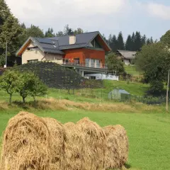 Nowoczesna zabudowa zagrodowa, kto może budować? Dom z panelami słonecznymi i drewnianą elewacją na wzgórzu, obok stogi siana.