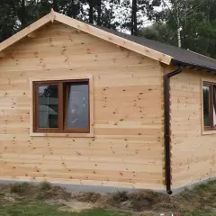 Drewniany domek letniskowy w trakcie budowy, z brązowymi oknami i dachem.