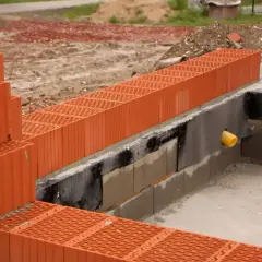 Budowa domu, widoczne pomarańczowe pustaki ceramiczne. Trwa układanie ścian fundamentowych, zastanawiasz się, ile suporexu na m2 będzie potrzebne?