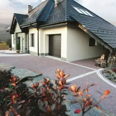 Piękny podjazd do domu z kostki brukowej, otoczony kamieniami i zielenią.
