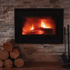 Płonące polana w nowoczesnym kominku, obok stos drewna i akcesoria. Widać, że można palić w kominku, tworząc przytulną atmosferę.