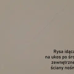 Pionowe pęknięcia ścian nośnych widoczne na jasnej powierzchni. Rysa biegnie ukośnie przez środek zewnętrznej ściany nośnej.