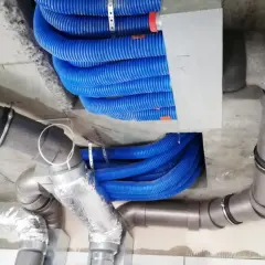 Instalacja rekuperacji w starym domu. Niebieskie przewody wentylacyjne i szare rury tworzą skomplikowany system pod sufitem.