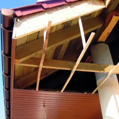 Widok od spodu na konstrukcję dachu z widoczną podbitką dachową na krokwiach, kominem i rynną.