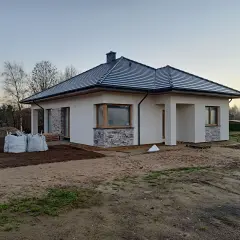 Nowy, nowoczesny dom w renklodach 15 z szarym dachem i białymi ścianami, otoczony placem budowy.