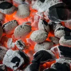 Żarzące się węgle i niedopalony ekogroszek w popielniku, tworzące gorącą, pomarańczową poświatę.