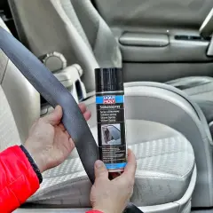 Ręce trzymające pas bezpieczeństwa i puszkę z napisem "Silikonspray". Preparat ten to olej silikonowy do paneli, który ułatwia konserwację wnętrza samochodu.