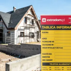 Tablica informacyjna budowy domu w trakcie prac, z widocznymi rusztowaniami. Na tablicy dane dotyczące budowy, adresu i kontaktów.