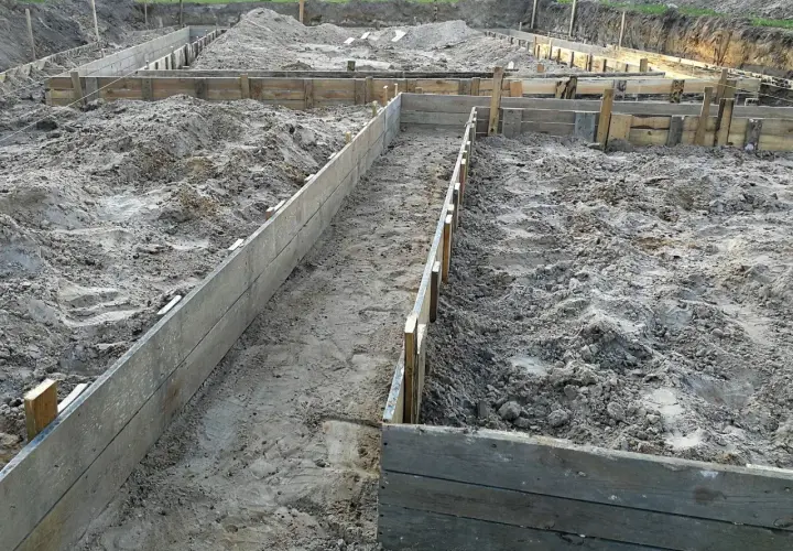 Wykonano wykopy pod fundamenty. Drewniane szalunki wyznaczają kształt przyszłego budynku na piaszczystym terenie budowy.