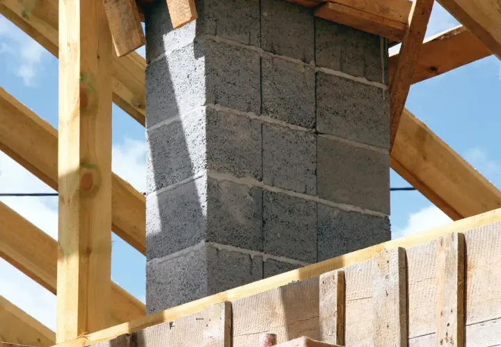 Solidny fundament pod komin systemowy, wznoszony z bloczków betonowych, otoczony drewnianą konstrukcją dachu.