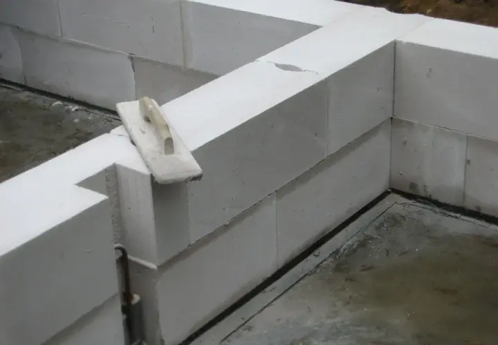 Ściana z bloczków z betonu komórkowego w trakcie budowy. Na jednym z bloczków leży kielnia.