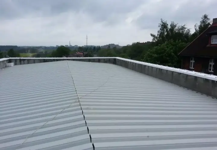 Szary, lekki dach płaski z blachy falistej, z widokiem na miasto w tle.