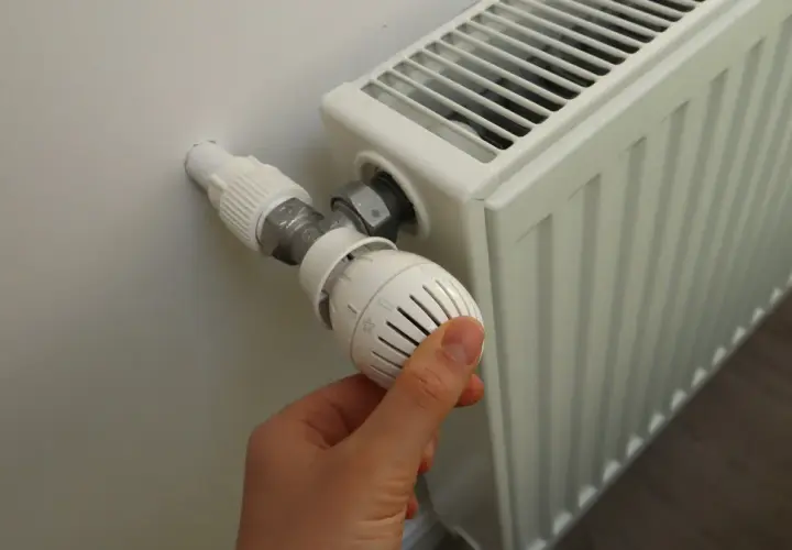 Dłoń reguluje termostat grzejnika. Sezon grzewczy od kiedy do kiedy zależy od pogody i przepisów.