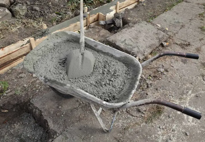 Taczka z betonem i łopatą czeka na wykonanie zbrojenia ławy fundamentowej.