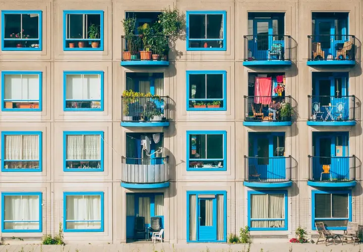 Elegancka loggia i balkon z niebieskimi ramami okiennymi, pełne zieleni i suszącego się prania, tworzą barwny obraz miejskiego życia.