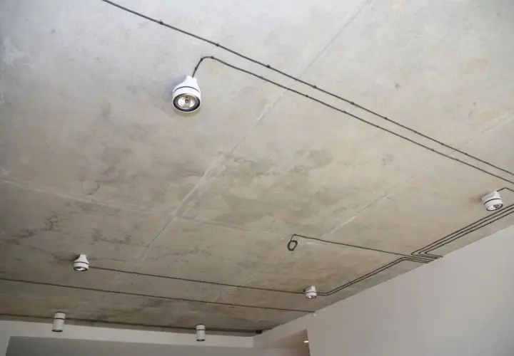 Nowoczesna instalacja elektryczna natynkowa na betonowym suficie z kilkoma białymi oprawami oświetleniowymi.
