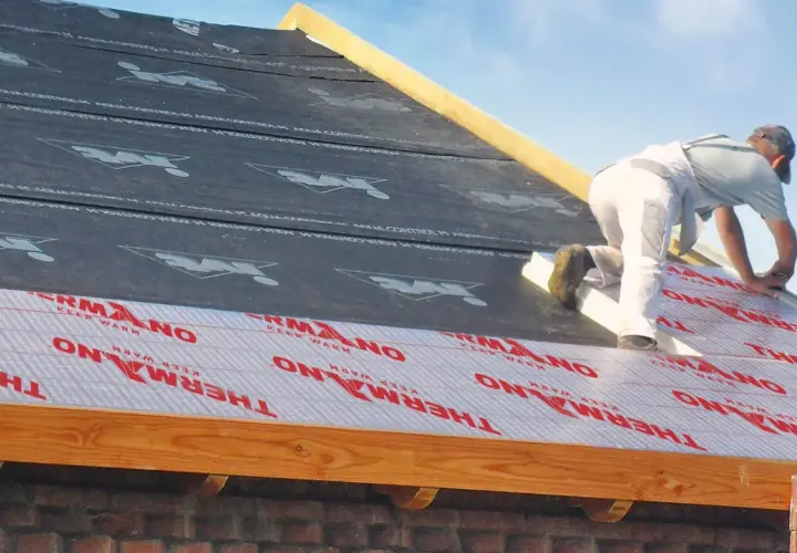 Pracownik montuje materiał izolacyjny na dachu, zapewniając ocieplenie dachu od zewnątrz.