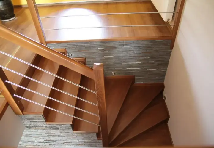 Eleganckie drewniane schody z metalową balustradą, prowadzące do górnego poziomu. Kamienna ściana stanowi stylowe tło, pokazując, jak zakończyć ostatni stopień schodów.